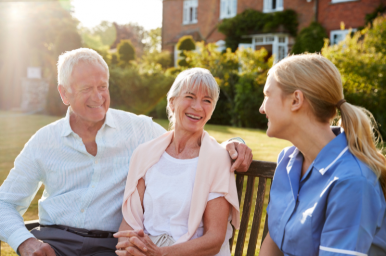 Seniors enjoying a warm conversation with a caregiver in a garden setting, emphasizing companionship and support in Alzheimer's and dementia care.