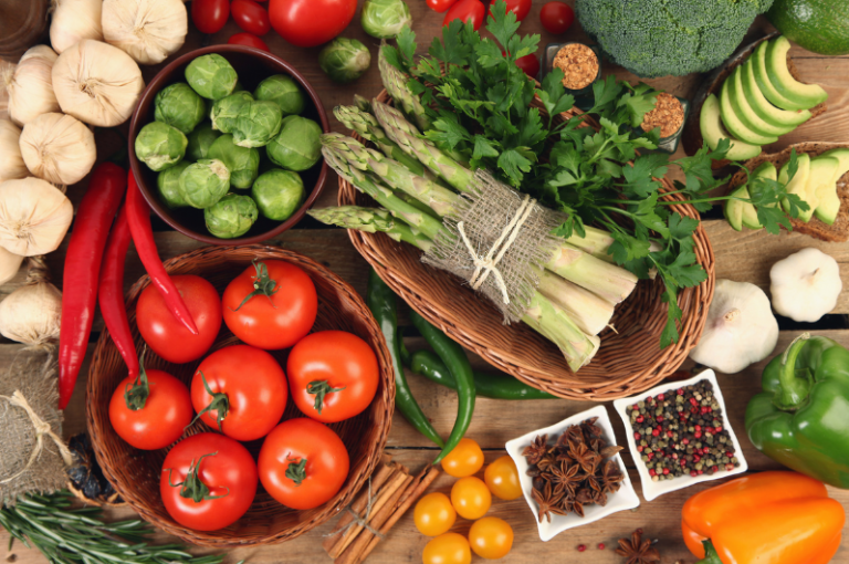Fresh vegetables including tomatoes, asparagus, bell peppers, and Brussels sprouts arranged on a wooden surface, highlighting healthy nutrition for seniors.