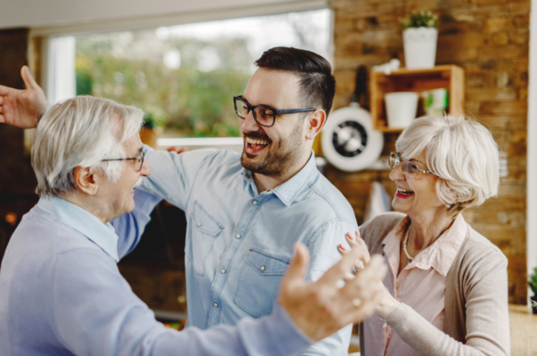Senior man and woman joyfully interacting with a younger man in a cozy kitchen setting, emphasizing family connection and support in senior care.