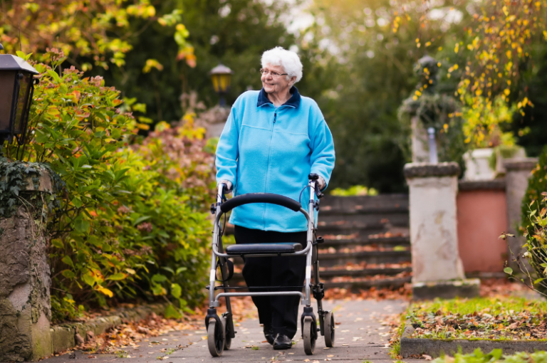 Elderly woman using a walker in a garden setting, surrounded by autumn foliage, promoting mobility and outdoor activity for seniors.