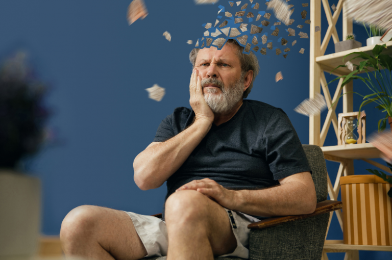 Senior man sitting in a chair, looking contemplative and distressed, with fragments symbolizing memory loss or cognitive decline, reflecting themes of aging and mental health in senior care.