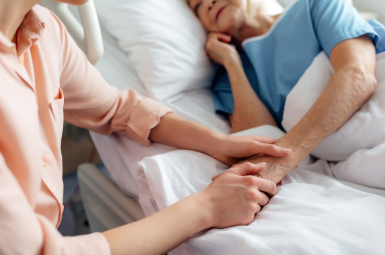 Caregiver holding the hand of a senior woman in a hospital bed, emphasizing compassion and support in healthcare settings.