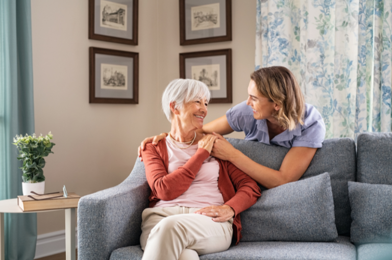 Senior woman and caregiver sharing a joyful moment on a couch in a cozy living room, emphasizing companionship and emotional support in caregiving.