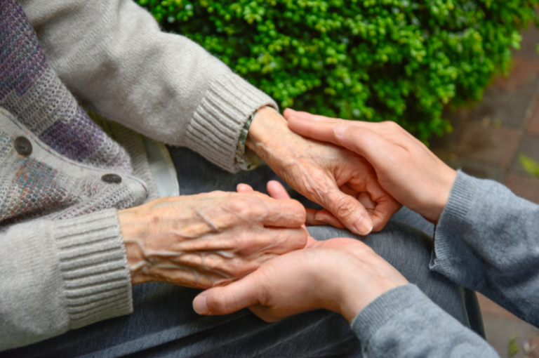 Elderly hands holding younger hands in a caring gesture, symbolizing support and connection in senior care.