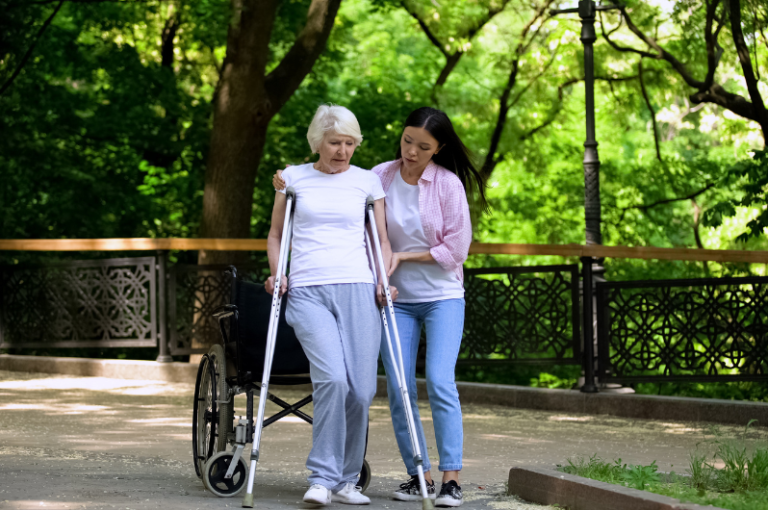 Elderly woman using a walker assisted by a caregiver in a park, emphasizing support for seniors' mobility and safety.
