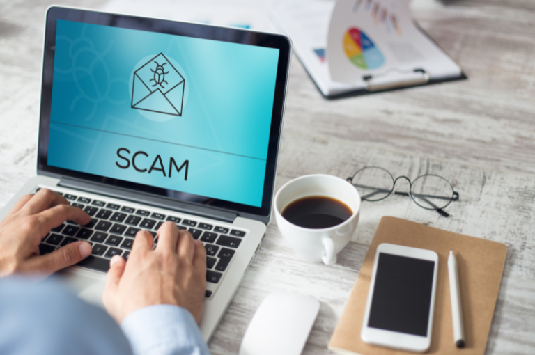 Person typing on laptop displaying "SCAM" alert, highlighting concerns about insurance scams targeting seniors, with coffee cup and smartphone nearby.
