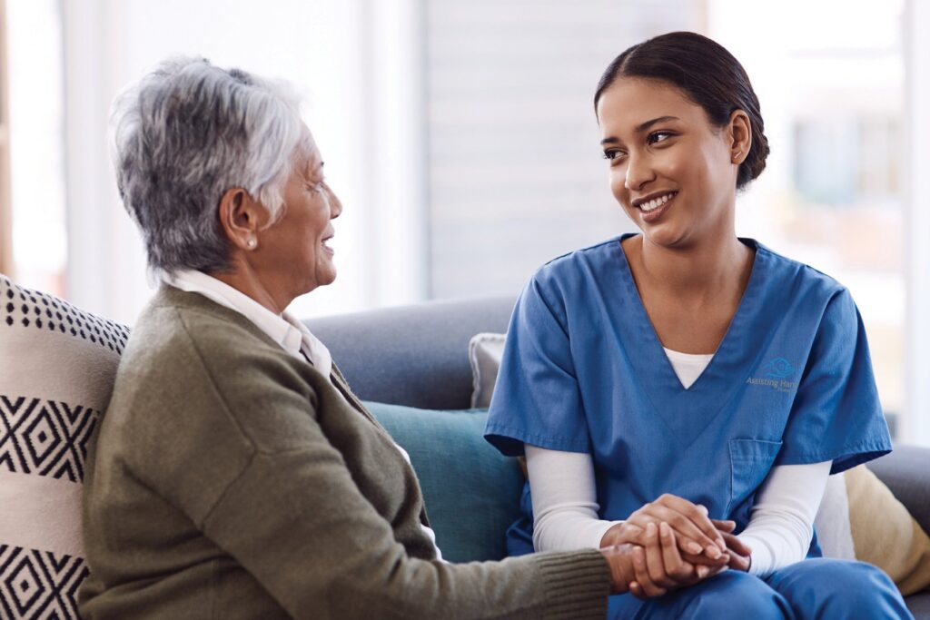 Caregiver in blue scrubs engaging with senior client, offering compassionate support and companionship in a comfortable home setting.